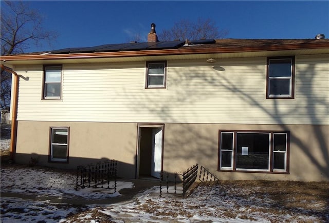 snow covered property with roof mounted solar panels and a chimney