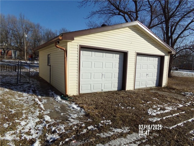 snow covered garage featuring fence and a detached garage