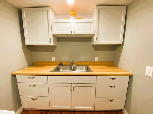 kitchen with butcher block countertops, a sink, white cabinetry, and baseboards