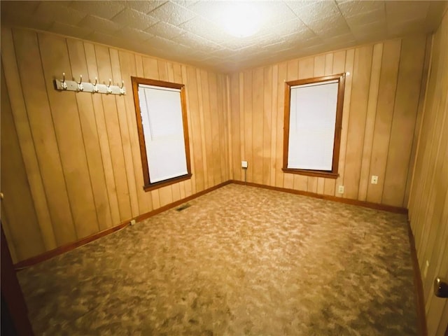 empty room featuring wood walls, baseboards, visible vents, and carpet flooring