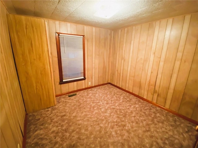 carpeted empty room featuring wood walls, baseboards, and visible vents