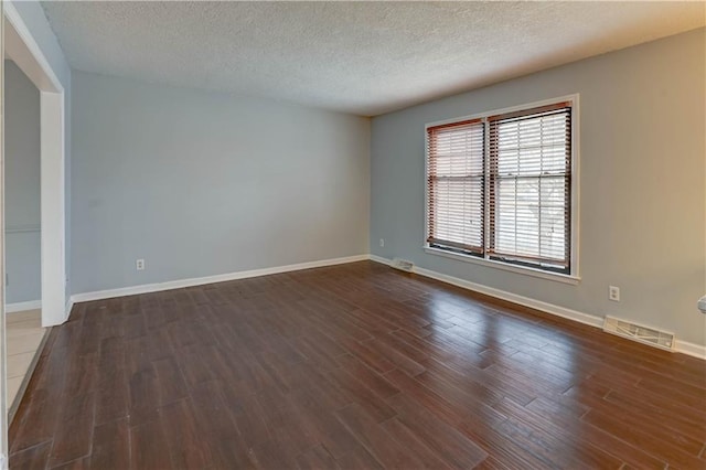 unfurnished room with baseboards, visible vents, dark wood finished floors, and a textured ceiling