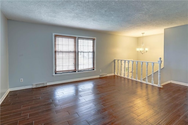 spare room with baseboards, a notable chandelier, visible vents, and dark wood-style flooring