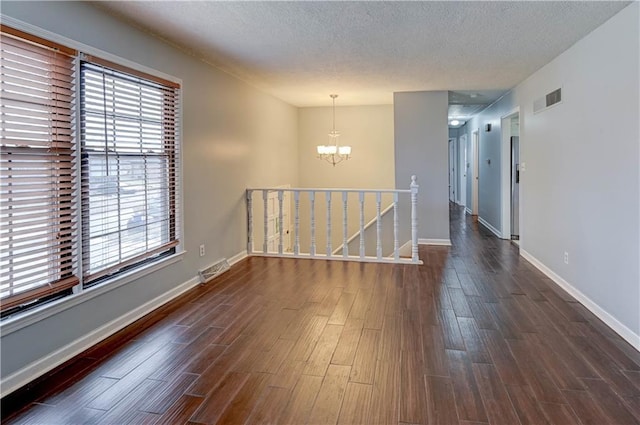 empty room featuring a textured ceiling, visible vents, dark wood finished floors, and a notable chandelier