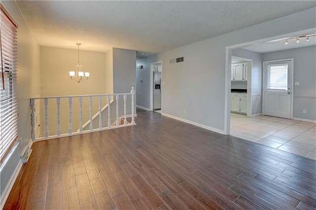 empty room featuring a textured ceiling, visible vents, baseboards, light wood finished floors, and an inviting chandelier