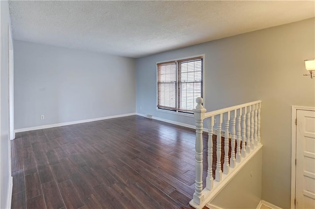 empty room with dark wood-style floors, a textured ceiling, and baseboards