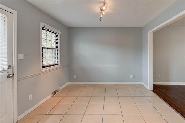 empty room featuring light tile patterned floors, baseboards, visible vents, and rail lighting