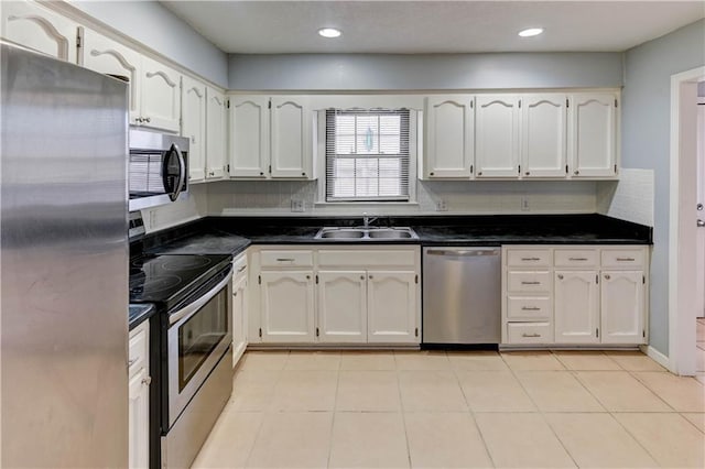 kitchen featuring decorative backsplash, white cabinets, dark countertops, appliances with stainless steel finishes, and a sink