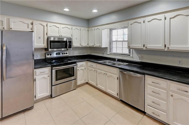 kitchen with dark countertops, white cabinetry, stainless steel appliances, and a sink