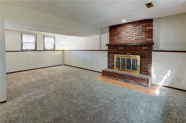 unfurnished living room featuring a fireplace, visible vents, carpet flooring, a textured ceiling, and baseboards