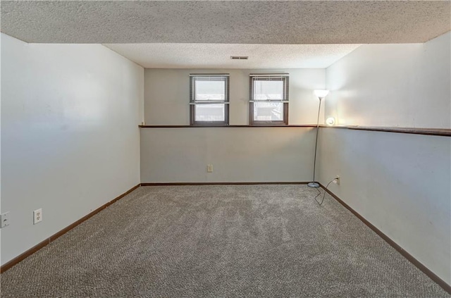 carpeted spare room featuring a textured ceiling, visible vents, and baseboards