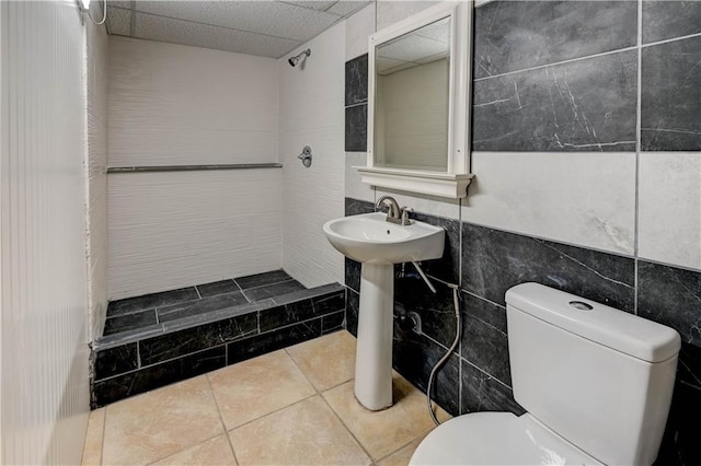 bathroom featuring tile walls, a paneled ceiling, toilet, a shower stall, and tile patterned flooring