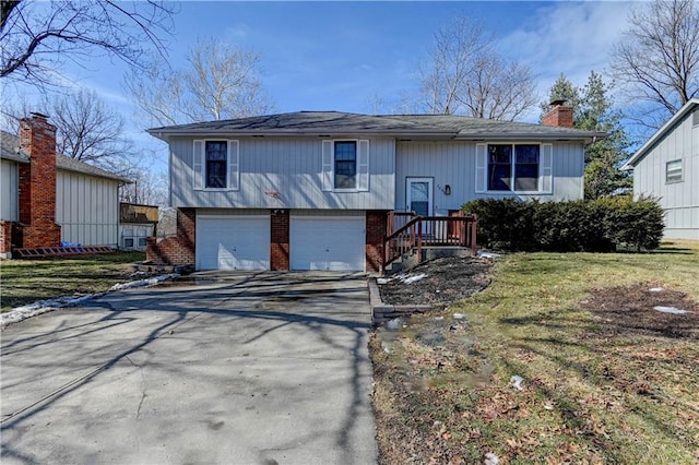 raised ranch featuring driveway, brick siding, a chimney, an attached garage, and a front yard