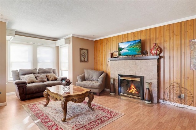 living area with a textured ceiling, a fireplace, wood finished floors, and crown molding