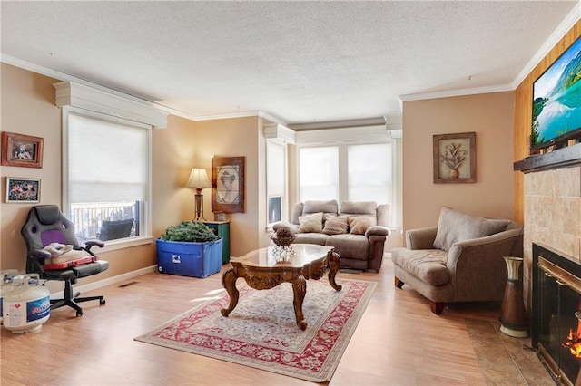 living room with a tile fireplace, crown molding, a textured ceiling, and wood finished floors