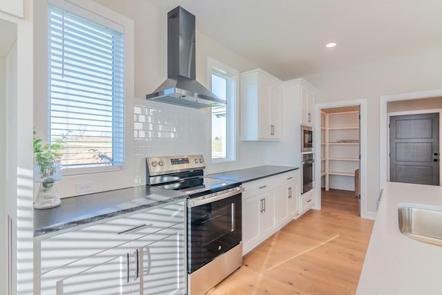 kitchen with dark countertops, stainless steel electric range, white cabinetry, and exhaust hood