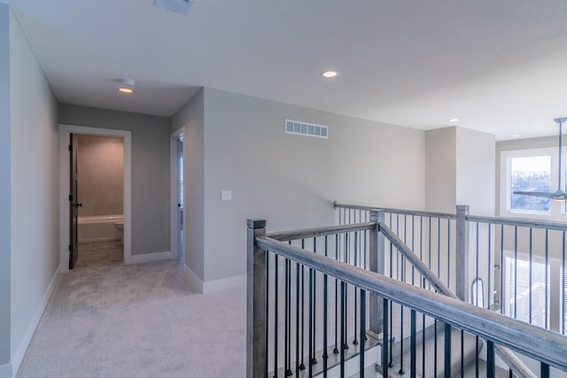 hall with baseboards, visible vents, light colored carpet, and an upstairs landing