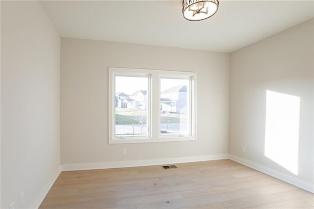 empty room featuring light wood-type flooring, visible vents, and baseboards