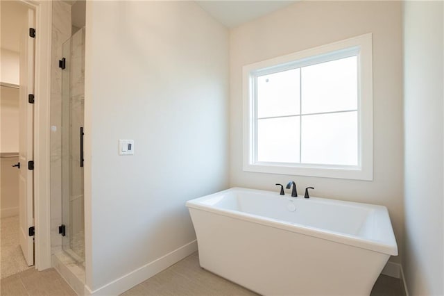 full bathroom featuring a stall shower, a soaking tub, a walk in closet, and baseboards