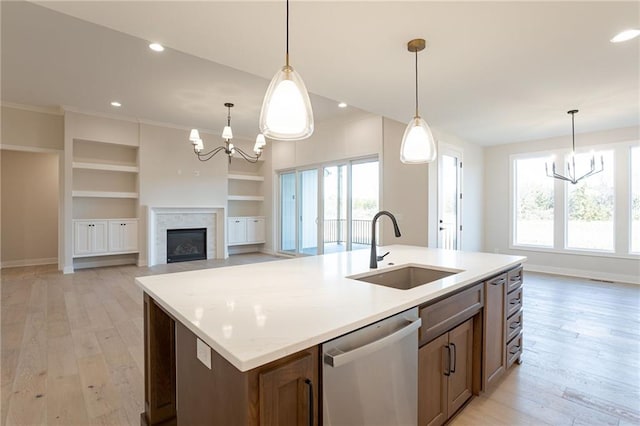 kitchen featuring stainless steel dishwasher, a sink, light wood-style floors, and a notable chandelier