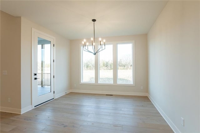 unfurnished dining area featuring a chandelier, baseboards, plenty of natural light, and light wood finished floors