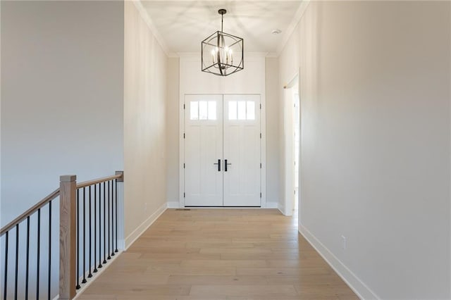 doorway featuring a notable chandelier, crown molding, light wood-style flooring, and baseboards