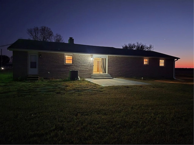 back of house at dusk featuring entry steps, a lawn, a patio area, and cooling unit