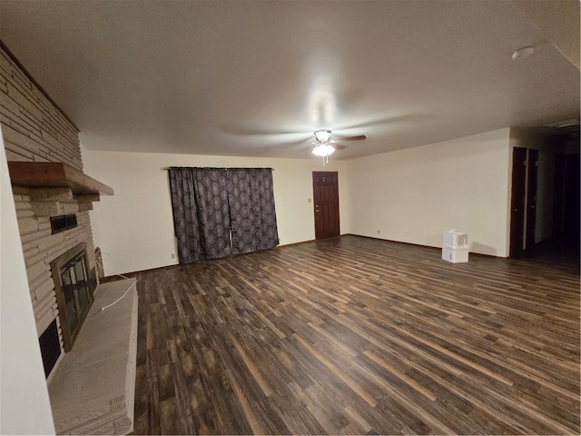 unfurnished living room with dark wood-type flooring, a stone fireplace, and a ceiling fan