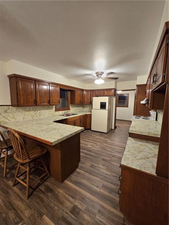 kitchen with dark wood-style flooring, light countertops, backsplash, white appliances, and a peninsula