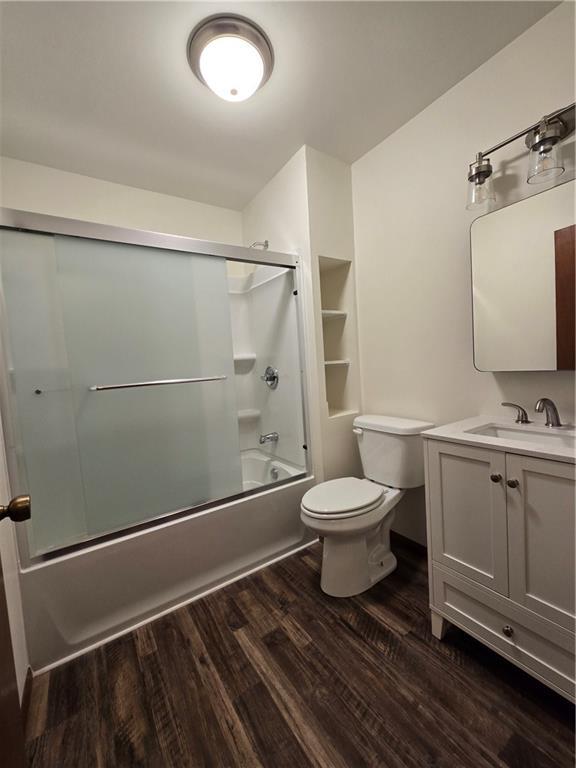 bathroom with toilet, shower / bath combination with glass door, wood finished floors, and vanity