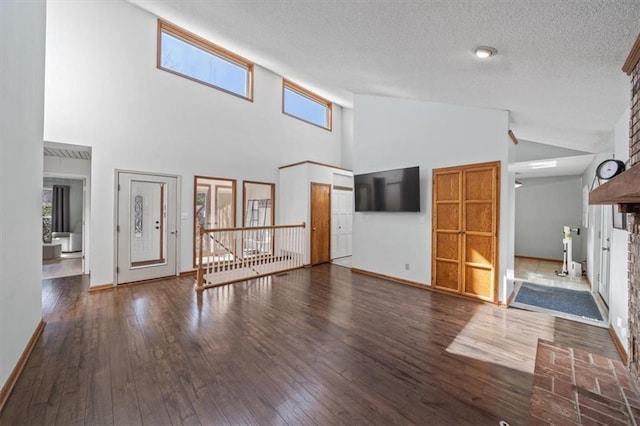 unfurnished living room featuring a textured ceiling, high vaulted ceiling, a fireplace, baseboards, and hardwood / wood-style floors