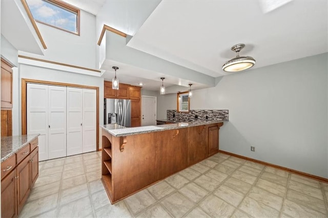 kitchen with a peninsula, light stone countertops, light floors, brown cabinetry, and stainless steel fridge