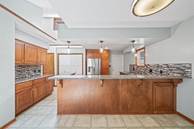 kitchen with light stone counters, brown cabinets, and stainless steel refrigerator with ice dispenser