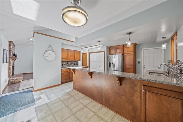 kitchen with brown cabinetry, a sink, stainless steel refrigerator with ice dispenser, and light stone counters