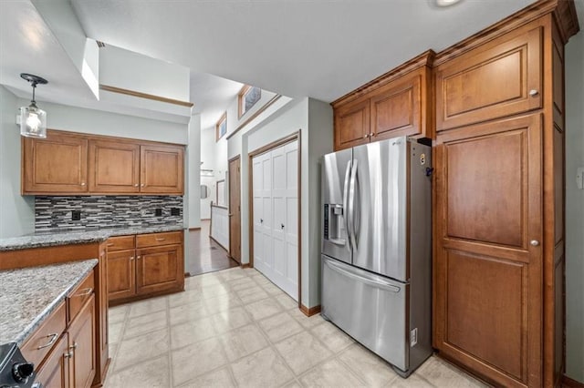 kitchen featuring brown cabinetry, stainless steel fridge, backsplash, and light stone counters