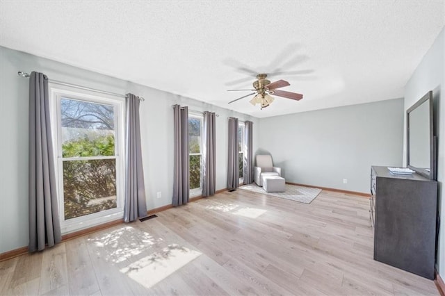 unfurnished room with a textured ceiling, ceiling fan, light wood-type flooring, and baseboards