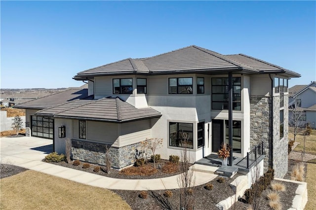 prairie-style house featuring stone siding, concrete driveway, a tile roof, and stucco siding