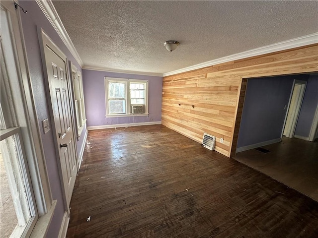 empty room featuring ornamental molding, a textured ceiling, wooden walls, and dark wood-style floors