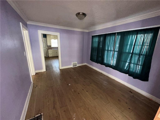 empty room featuring crown molding, visible vents, a textured ceiling, wood finished floors, and baseboards