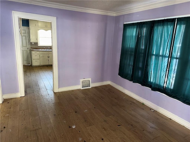 empty room with visible vents, crown molding, baseboards, and wood finished floors