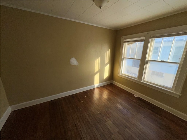 empty room featuring baseboards, dark wood finished floors, and ornamental molding