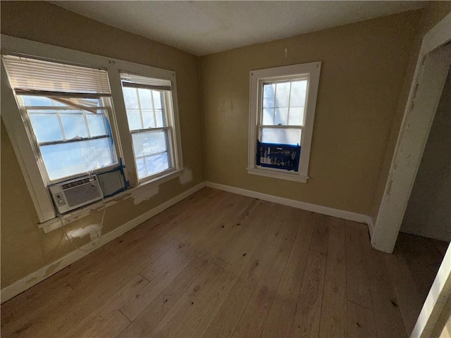 unfurnished room with light wood-type flooring, cooling unit, and baseboards