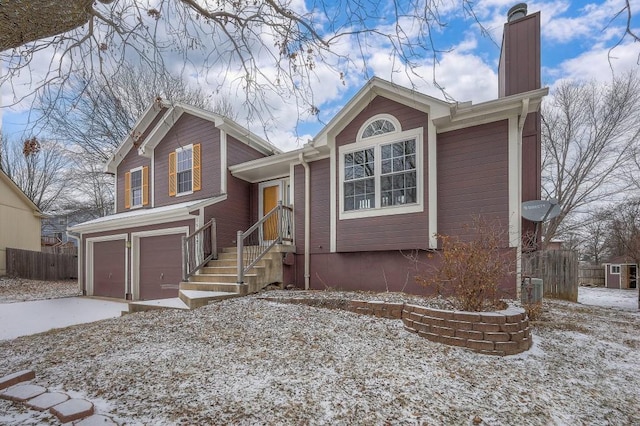 tri-level home with driveway, a chimney, an attached garage, and fence