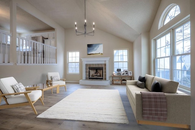 living room featuring a chandelier, high vaulted ceiling, a tiled fireplace, and wood finished floors