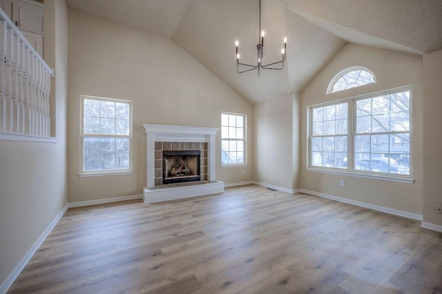 unfurnished living room with light wood-type flooring, a fireplace, a chandelier, and a wealth of natural light