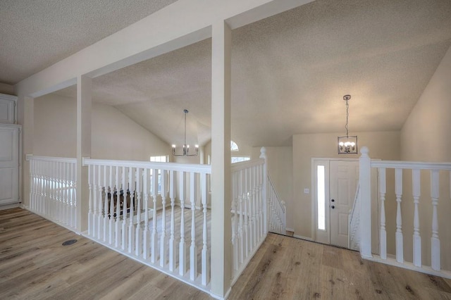 foyer entrance with a notable chandelier, light wood-style flooring, a healthy amount of sunlight, vaulted ceiling, and a textured ceiling