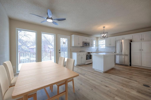 dining area featuring ceiling fan with notable chandelier, a textured ceiling, and light wood-style flooring