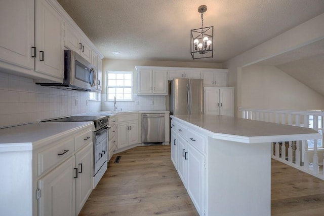 kitchen featuring white cabinets, a kitchen island, decorative light fixtures, stainless steel appliances, and light countertops