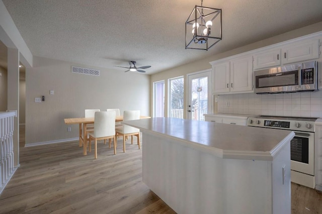 kitchen featuring white range with electric stovetop, pendant lighting, light countertops, stainless steel microwave, and white cabinets