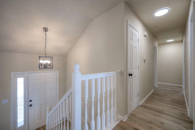 foyer with lofted ceiling, an inviting chandelier, light wood-style floors, a textured ceiling, and baseboards